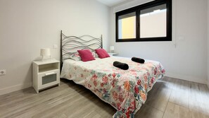 A bedroom with a bed, a nightstand, a window, and a wall socket. - View of Guanarteme Surf, Las Canteras 2 (Palmas De Gran Canaria, Las)