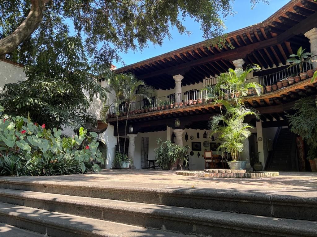 A courtyard with steps leading to a building with a balcony, surrounded by potted plants and trees.