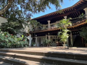 Un patio con escalones que llevan a un edificio con balcón, rodeado de plantas en macetas y árboles.
