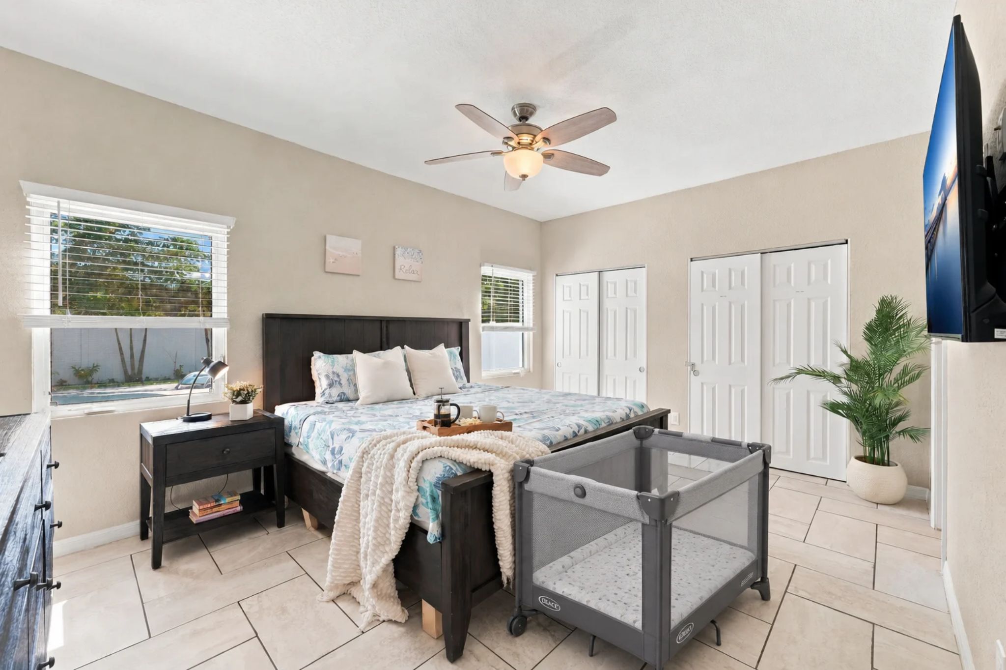 Bright main bedroom with a comfy bed, ceiling fan, and pack 'n play set up for little ones