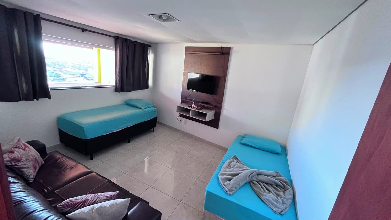 A small, compact room with two beds, a sofa, and a TV.