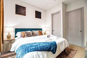 A hotel room with a bed, a nightstand, a lamp, a door, and two wall art pieces. - DT Sky Lounge|FirePit+PoolTbl+Golf+Sauna|Sleeps16 (Dallas)