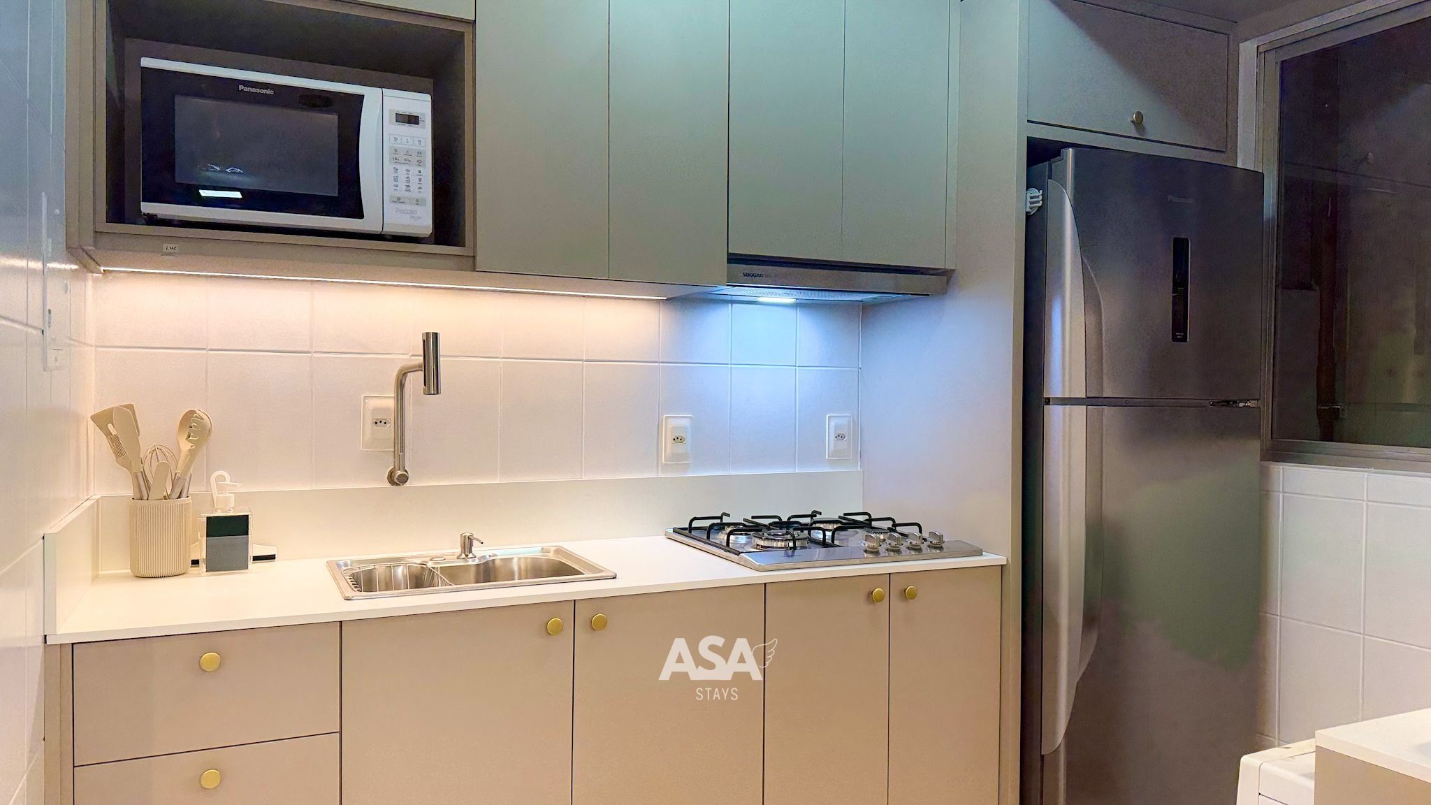 Una cocina con microondas, estufa a gas, refrigerador de acero inoxidable y un armario con la leyenda 'ASA STAYS'.