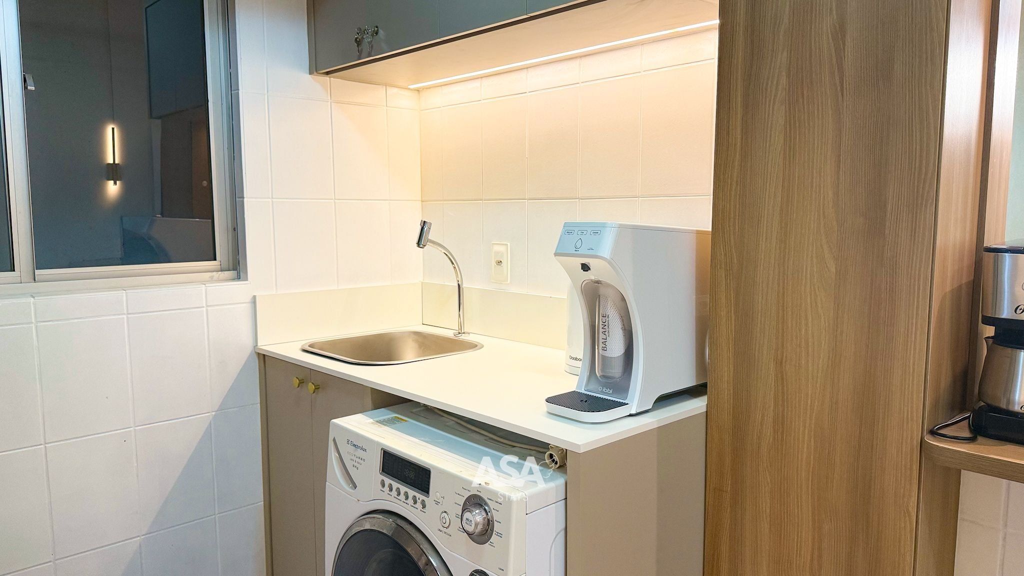 Cocina compacta con lavadora, cafetera y lavabo.