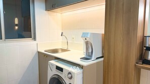 Cocina compacta con lavadora, cafetera y lavabo.