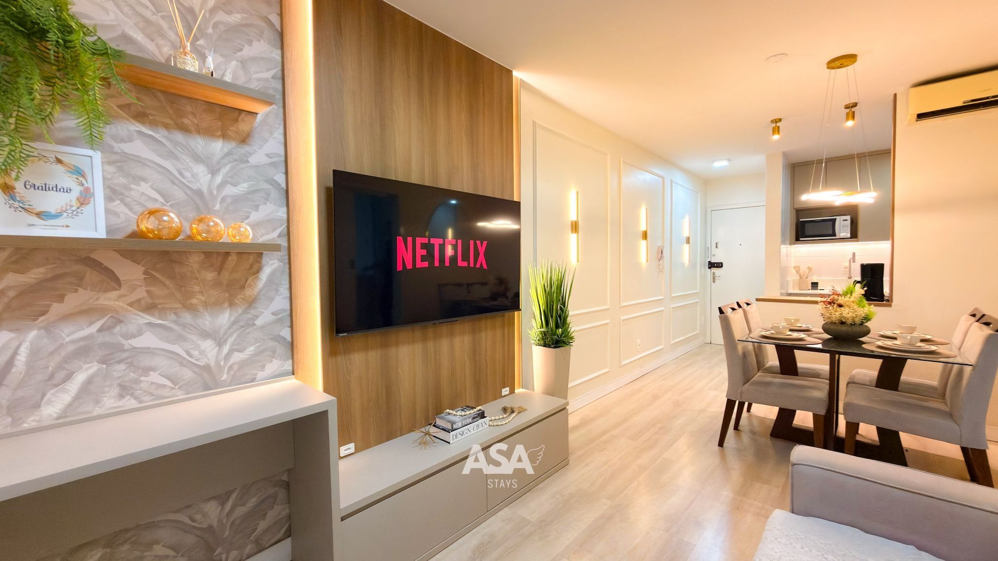 A modern living room with a flat-screen TV displaying 'NETFLIX', a dining area with a glass table, and a kitchen with a microwave.