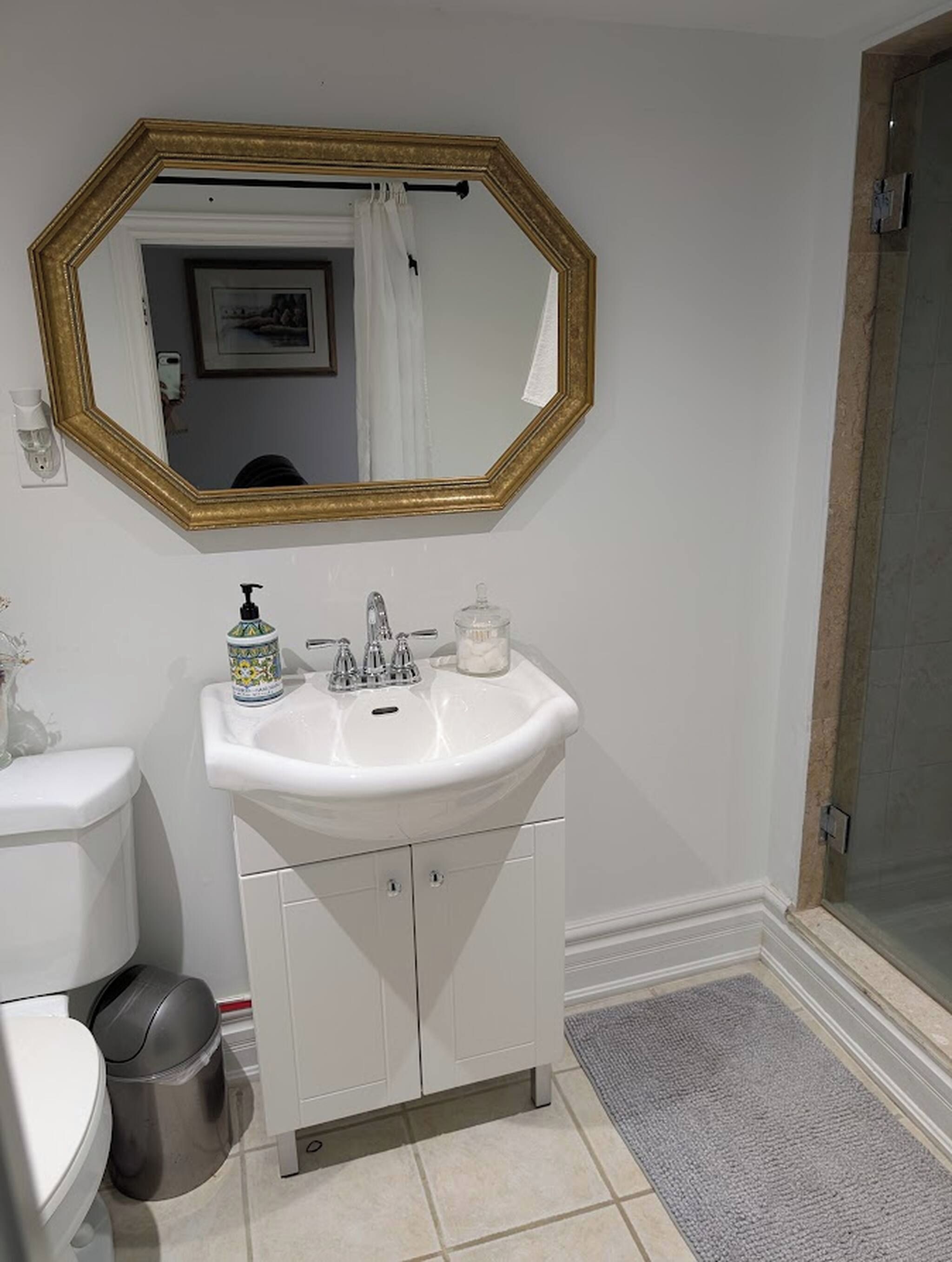 Un baño con lavamanos blanco, espejo con marco dorado y zona de ducha.