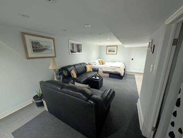 A modern bedroom with a black leather sofa, a bed with white bedding, and a small side table with a plant.