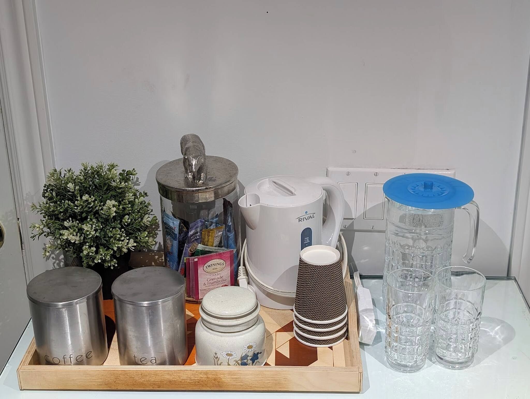 A kitchen counter with various items including a coffee maker, tea pot, jars, and glassware.