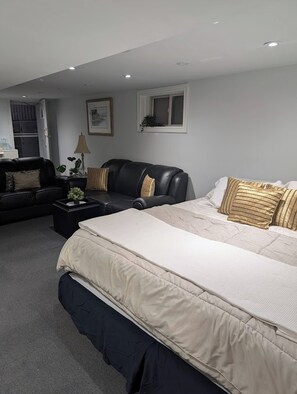 A bedroom with a large bed, a black leather sofa, and a small table with a lamp. - Room-king Size In-suite Basement (Toronto)