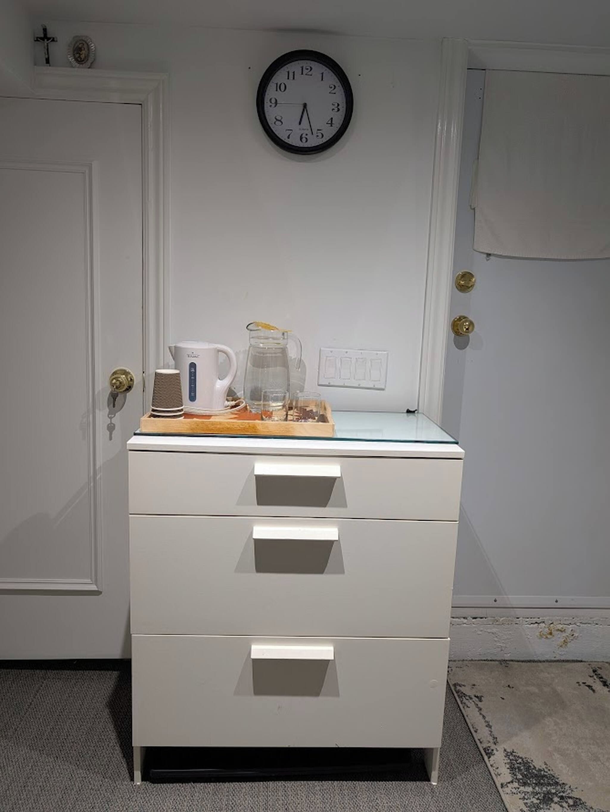 A white dresser with drawers, a clock on the wall, and a door with a brass handle.
