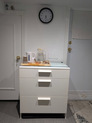 A white dresser with drawers, a clock on the wall, and a door with a brass handle. - Room-king Size In-suite Basement (Toronto)
