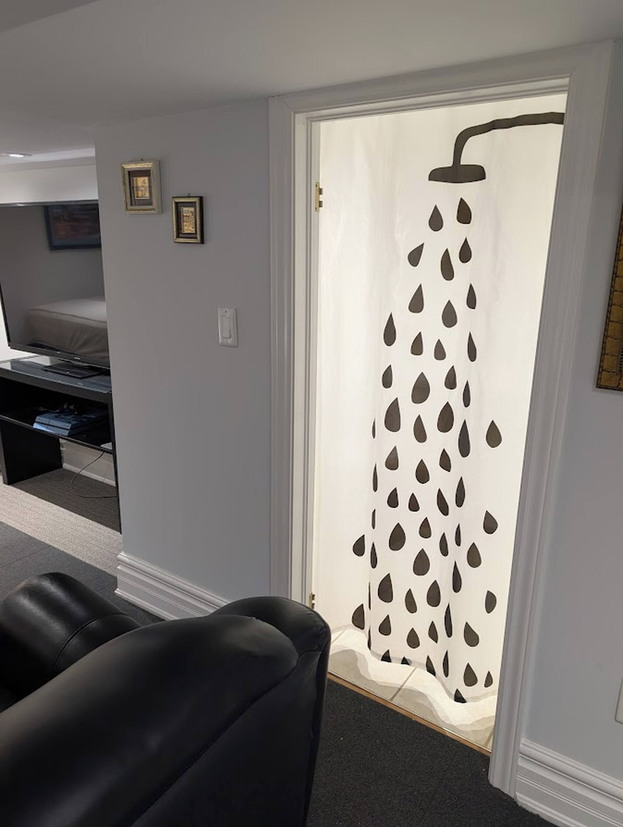A room with a shower curtain featuring a water droplet pattern, a black leather chair, and a small desk with a computer.