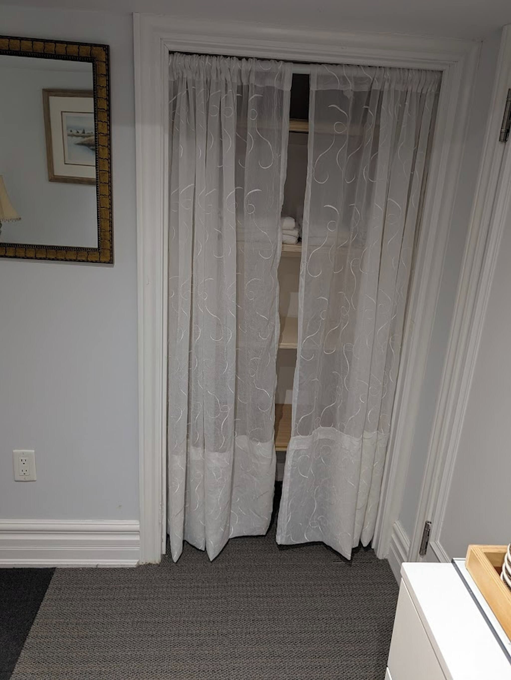 A room with a white door, a mirror on the wall, and a carpeted floor.