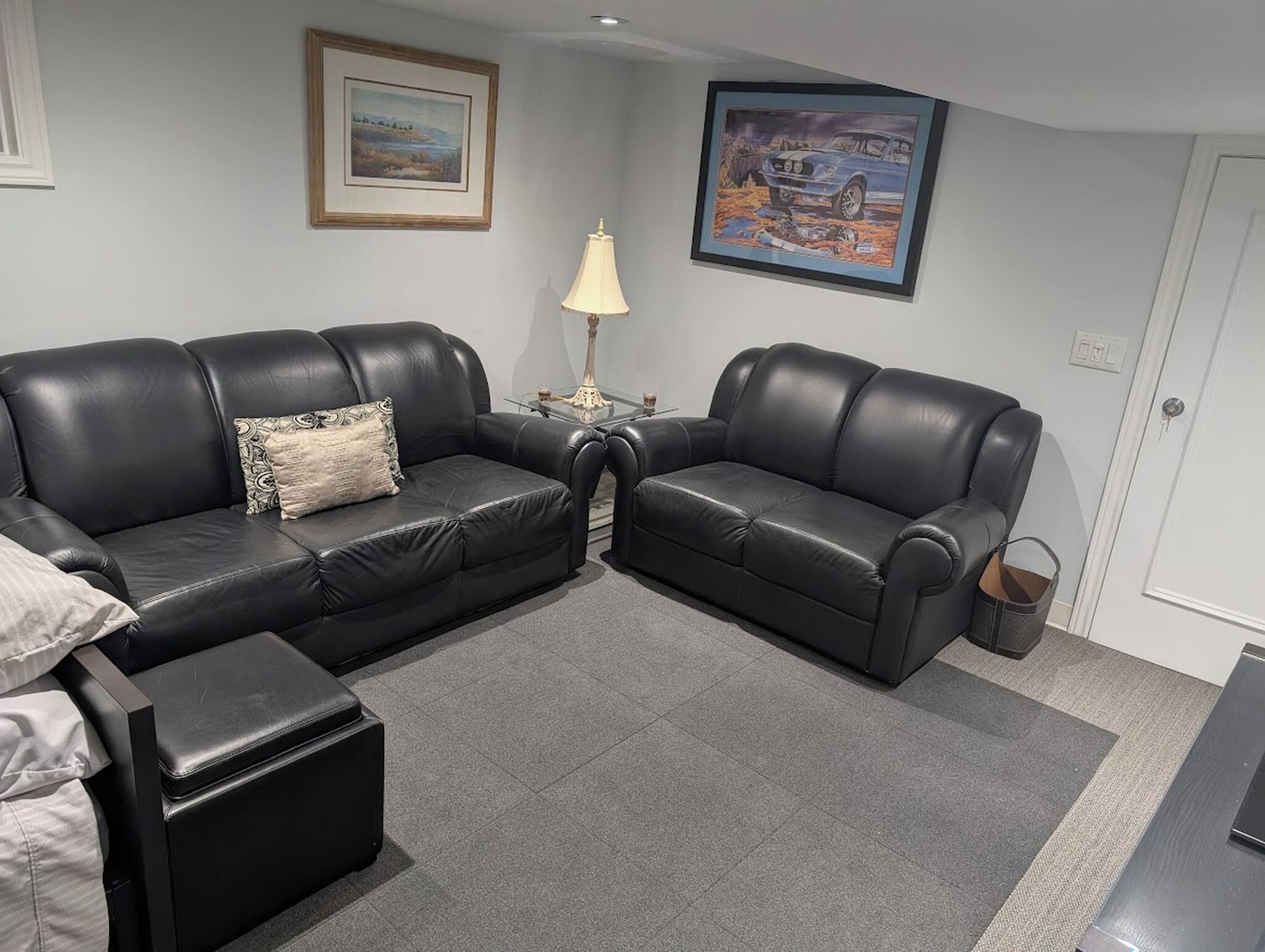 A living room with two black leather sofas, a small table with a lamp, and a framed picture on the wall.