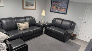 A living room with two black leather sofas, a small table with a lamp, and a framed picture on the wall.