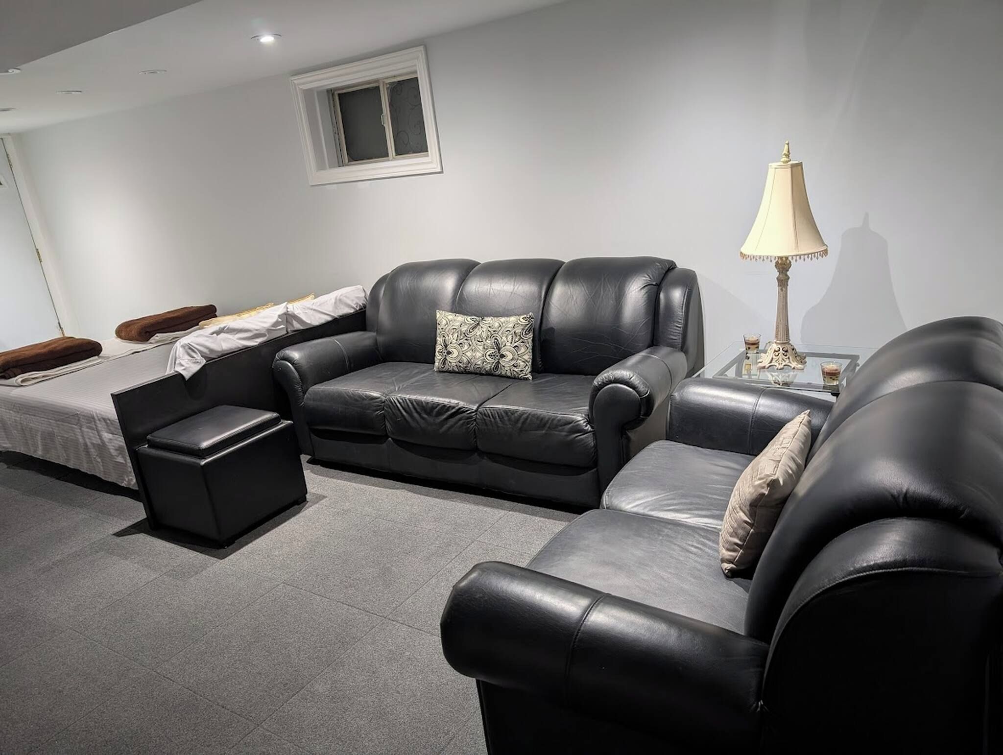 A modern living room with a black leather sofa, a glass coffee table, and a lamp.
