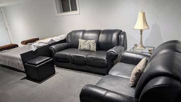 A modern living room with a black leather sofa, a glass coffee table, and a lamp.