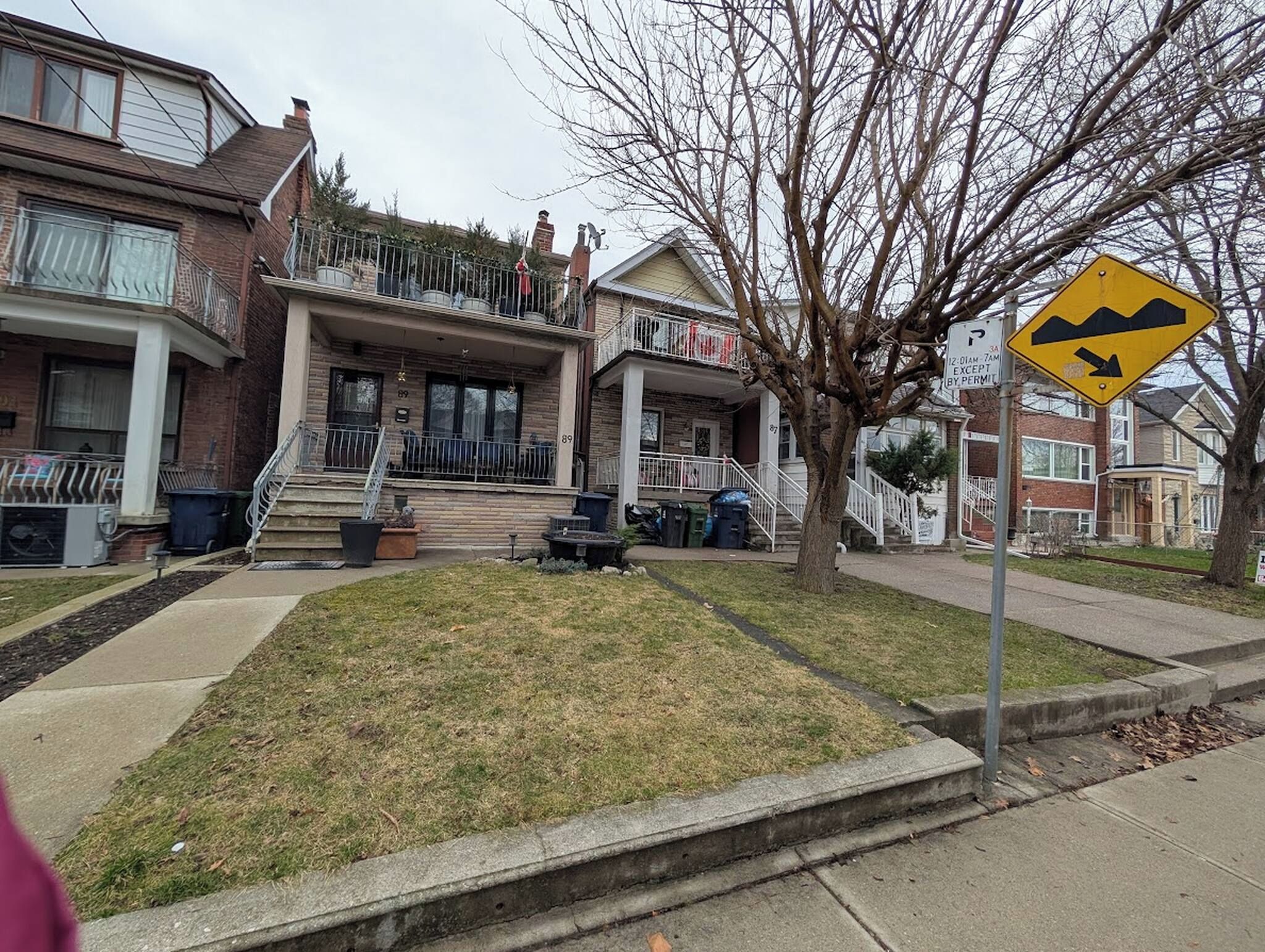 Una calle residencial con casas, un área con césped y un paso de peatones.