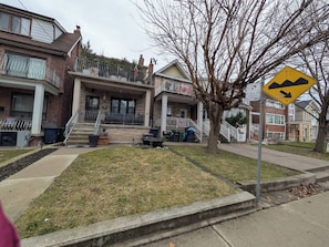 A residential street with houses, a grassy area, and a pedestrian crossing.