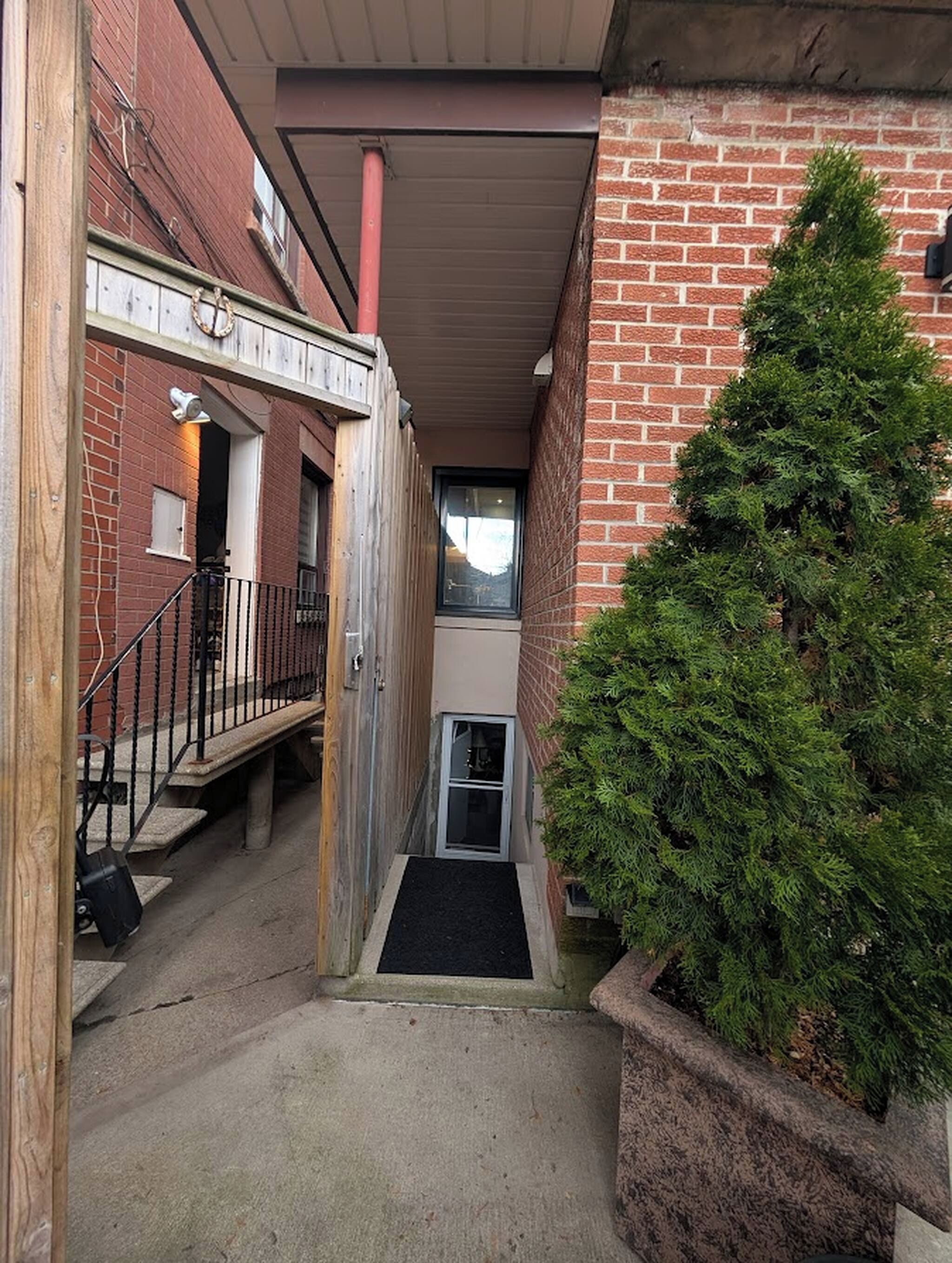 A narrow alleyway with a wooden fence, a metal gate, and a small door leading to a building with a brick exterior.