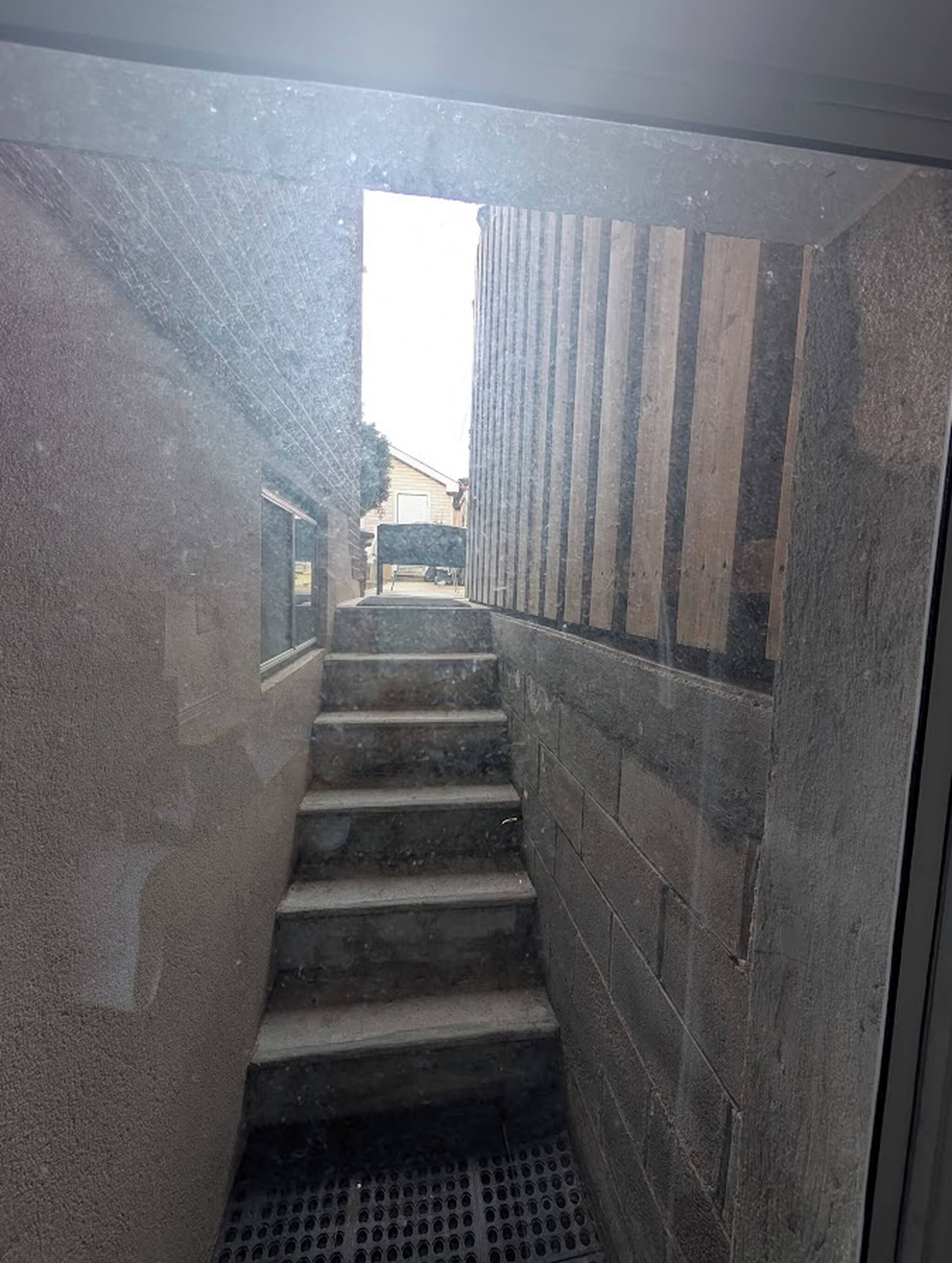 Una escalera estrecha con una reja metálica al final, que conduce a una puerta con listones de madera verticales.