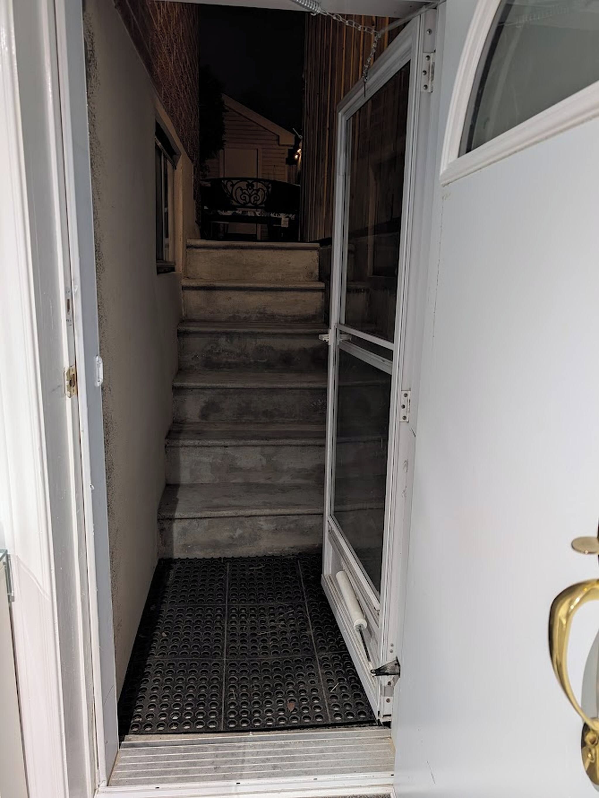 Un escalier étroit mène à une porte surmontée d’une grille métallique.