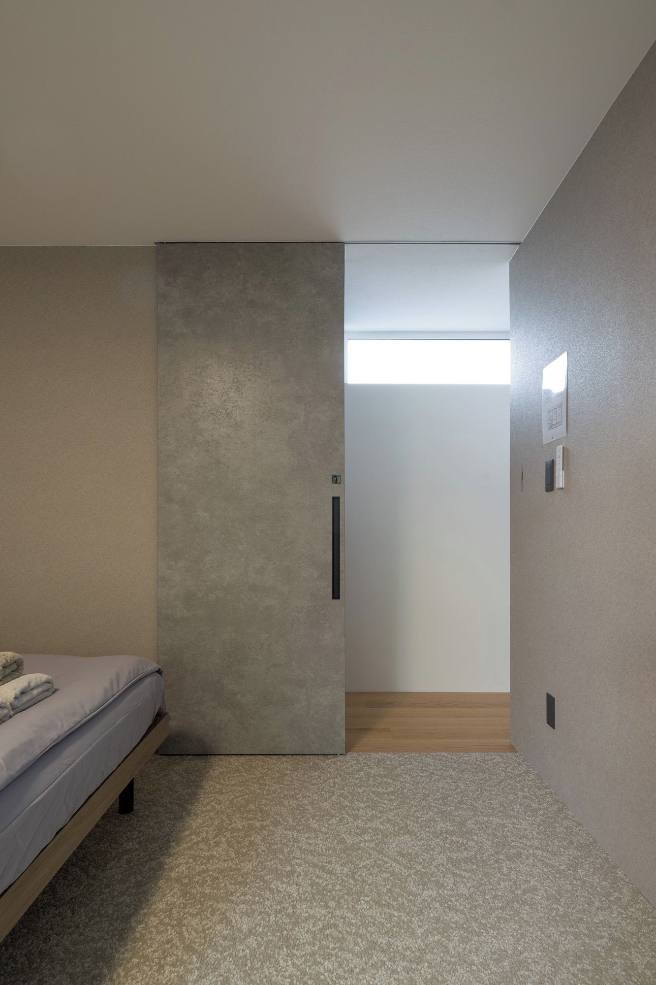 A bedroom with a bed, a sliding door, a light switch, and a wall-mounted light fixture.