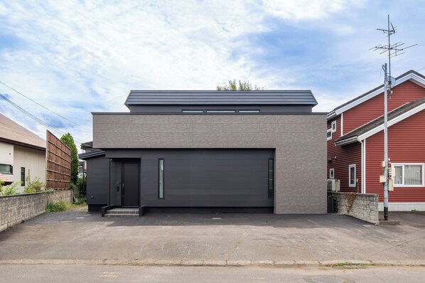Una casa moderna de dos pisos con puerta de garaje gris oscuro, techo plano y un pequeño alero.