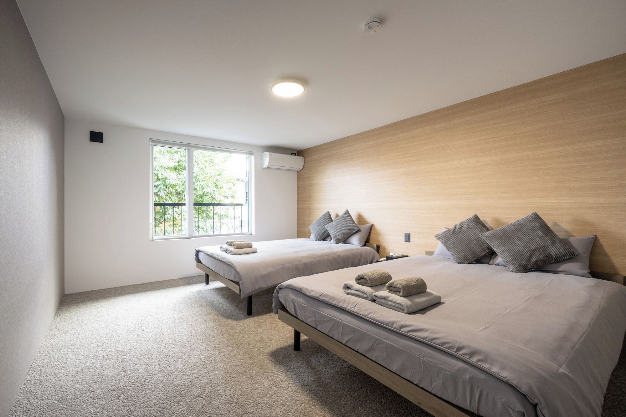 A modern bedroom with two beds, a large window, and a ceiling light.