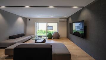 A modern living room with a glass coffee table, a sofa, a bean bag, and a flat-screen TV mounted on the wall.