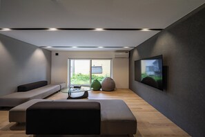 Una sala de estar moderna con una mesa de centro de vidrio, un sofá, un sillón de peluche y un televisor de pantalla plana montado en la pared.