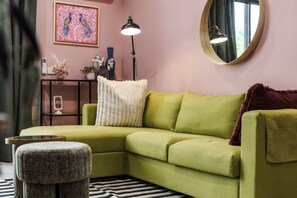 A green sofa with a white pillow, a round mirror, a black lamp, and a decorative painting on the wall. - Stylish 1-Bed Apartment with Outdoor Space (Kingston)