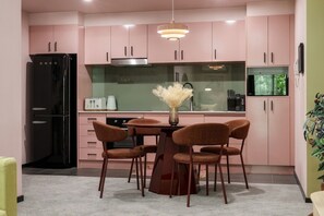 Een moderne keuken met roze kastjes, een zwarte koelkast, een eettafel met stoelen en een vaas met gedroogde bloemen.