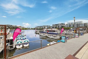 A marina with several boats docked, a wooden walkway, and modern buildings in the background. - Stylish 1-Bed Apartment with Outdoor Space (Kingston)