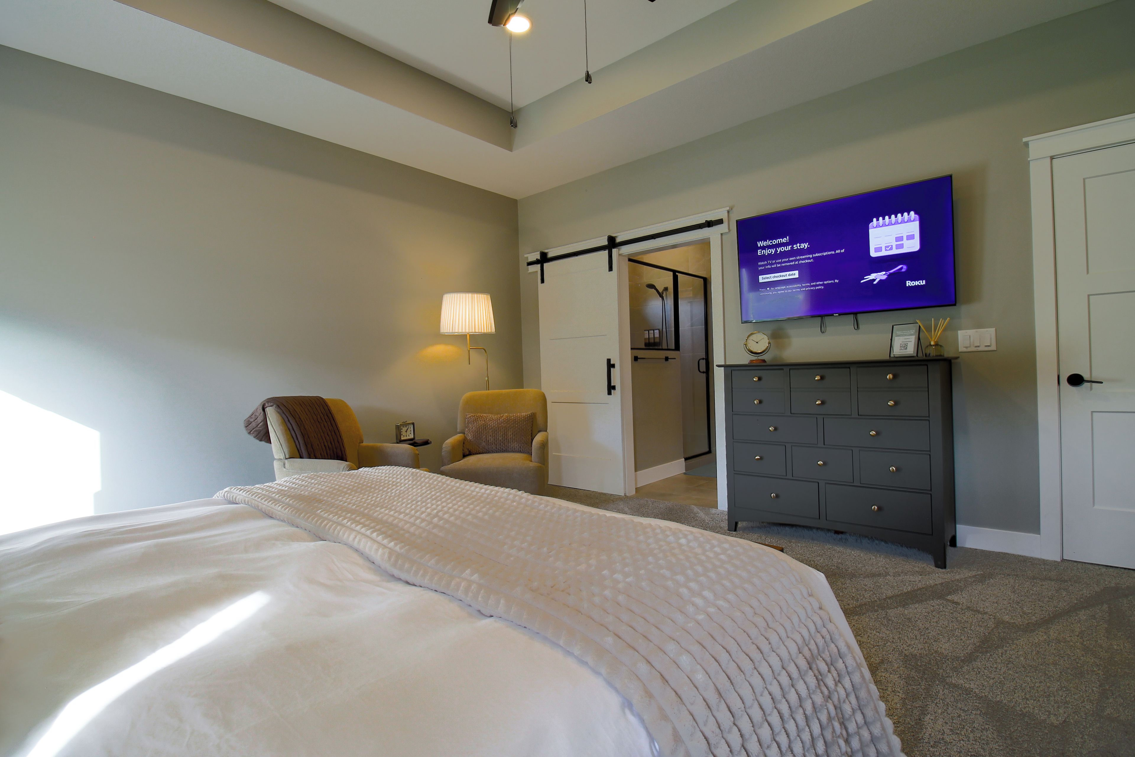 Habitación de hotel con cama, una silla, tocador y televisor mostrando un mensaje de bienvenida.