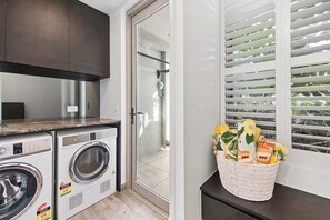A laundry area with a washing machine and dryer, a glass door leading to a shower, and a basket of towels on a windowsill. - The Esplanade, Palm Beach (Palm Beach)