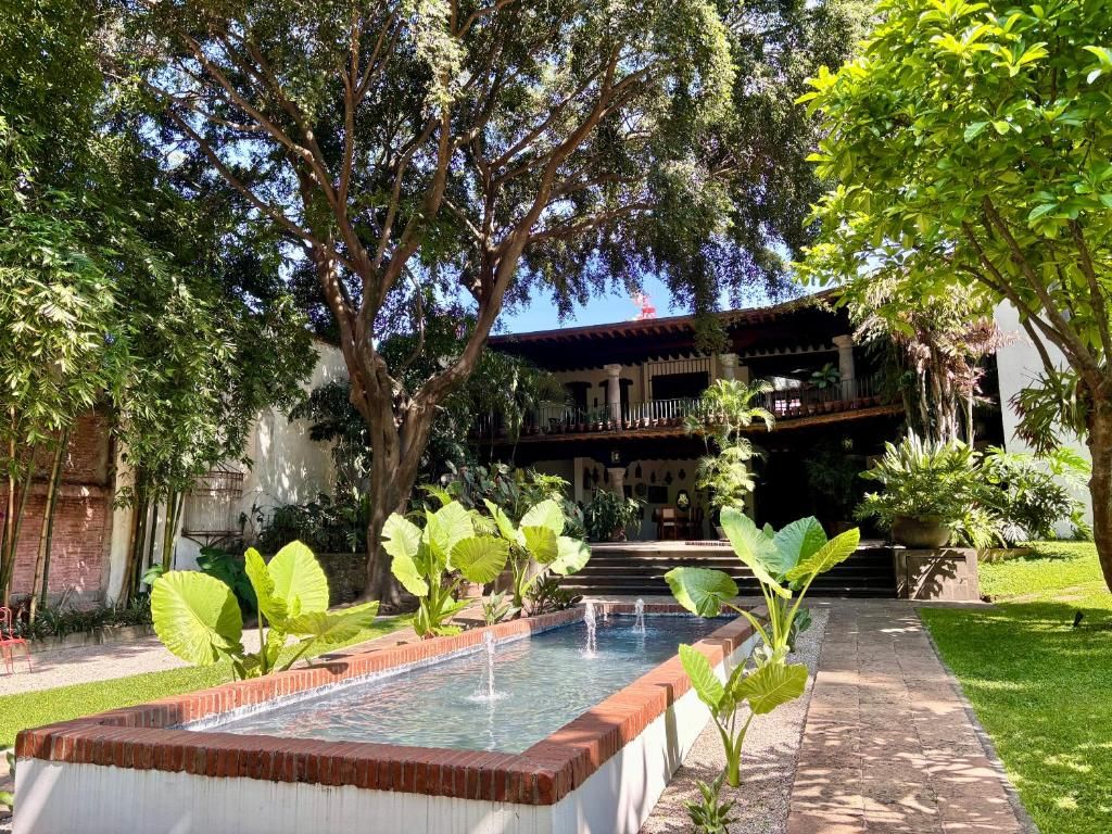 Une cour avec une piscine rectangulaire, entourée de grands arbres et d’un bâtiment doté d’un balcon.
