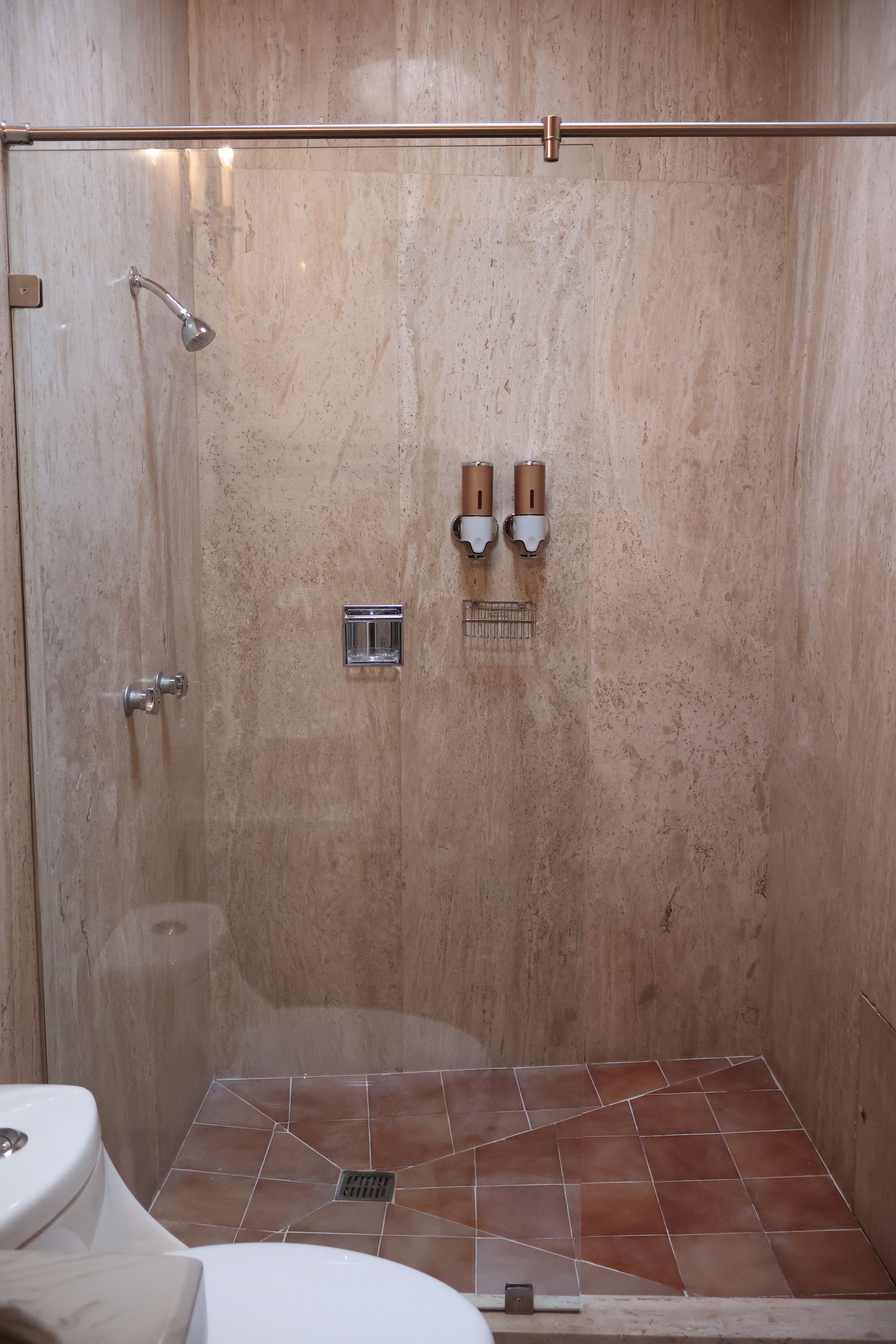 Une douche avec une porte en verre, un pommeau de douche à main et un robinet mural.