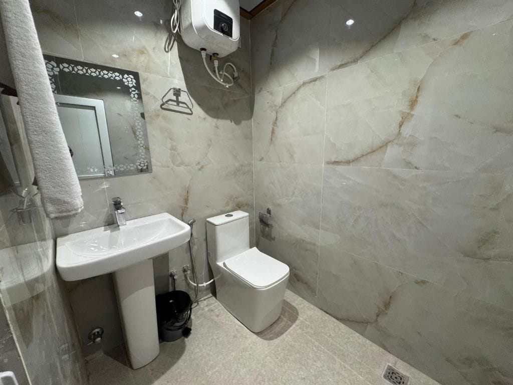 A bathroom with a marble wall, a sink, a toilet, and a towel rack.