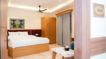 A hotel room with a bed, a wooden wardrobe, a ceiling fan, and a painting on the wall.