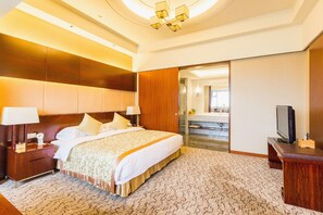 Una camera d'albergo con un letto grande, comodini, una televisione e un bagno visibile tramite una porta aperta.