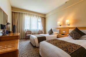 Una camera d'albergo con due letti, una scrivania, una sedia, una televisione e una finestra con tende.