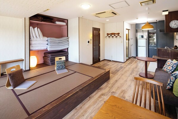 A modern hotel room with a tatami mat seating area, a wooden dining table, and a kitchenette.