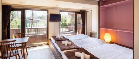 Habitación de hotel con cama, escritorio, silla, televisión y balcón.