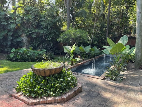 A garden with a water feature, a stone planter with plants, and a brick pathway.
