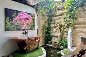 A rustic bathroom with a copper bathtub, a stone statue, and a wall-mounted painting of a rose. - Luxury Villa Near Ubud with Private Gym & Copper Bathtub_PARVATI (Kecamatan Ubud)