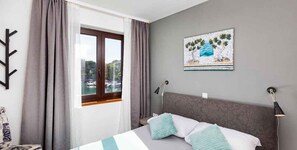 Ein Hotelzimmer mit einem Bett, einem Vorhangfenster, einem Bild an der Wand und einer Lampe.