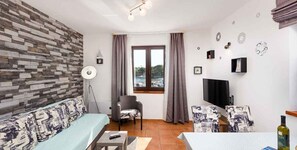 Ein Wohnzimmer mit Steinwand, einer Couch, einem Sessel, einem Fernseher und einem Fenster mit Vorhängen.