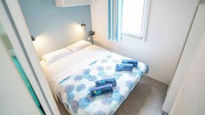 A small, neatly made bed with a patterned bedspread and two towels. - Mobile home with air conditioning, terrace and water park (Čatež ob Savi)